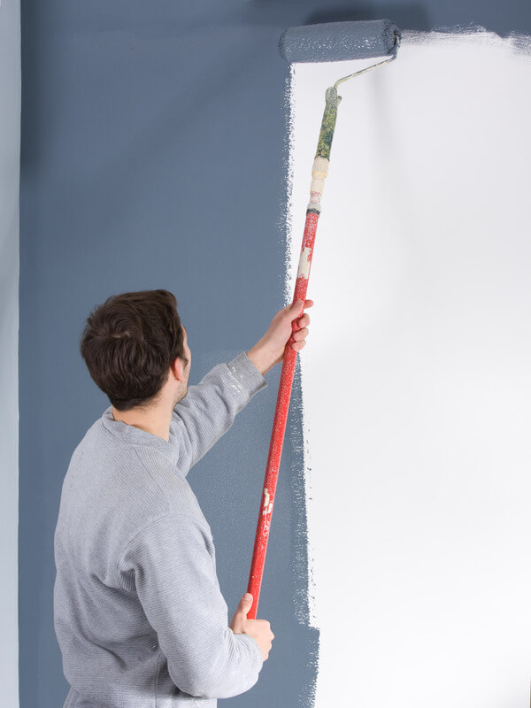 Painter in Richmond applying blue paint to a white wall using a paint roller